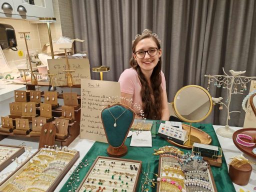 A smiling woman at a jewellery stall, surrounded by various handmade accessories.